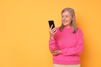 Photo of Senior woman with phone on orange background, space for text