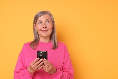 Photo of Senior woman with phone on orange background, space for text