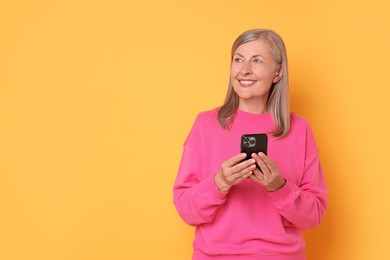 Senior woman with phone on orange background, space for text