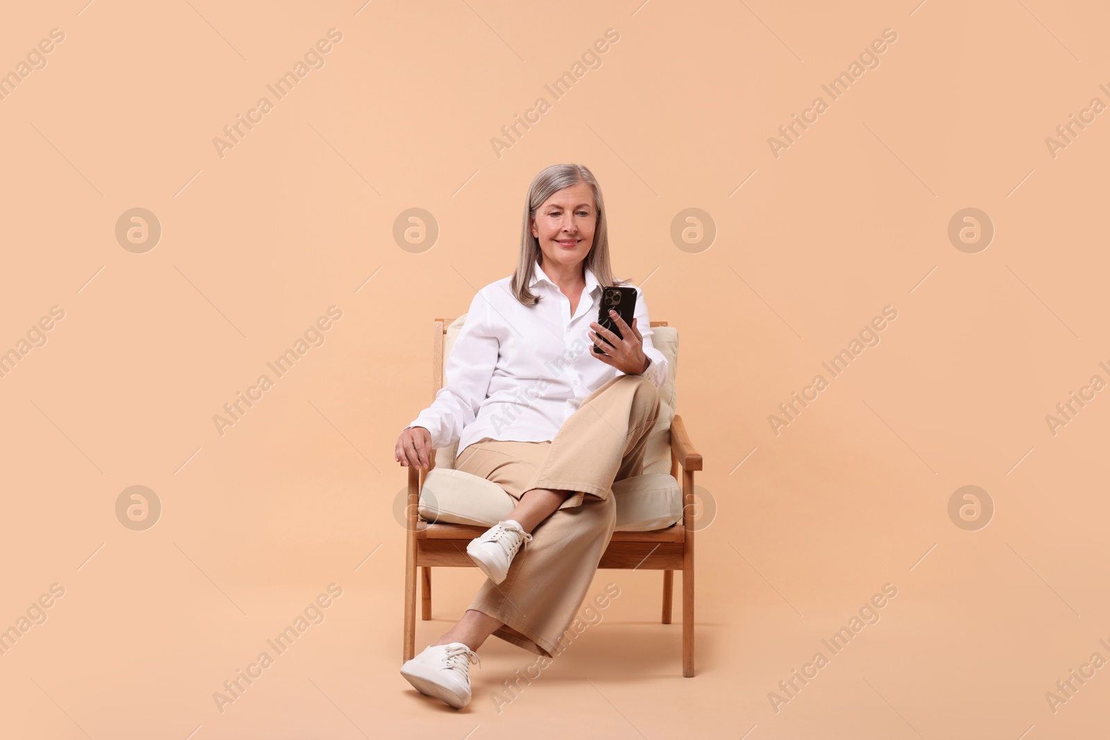 Photo of Senior woman with phone on armchair against beige background