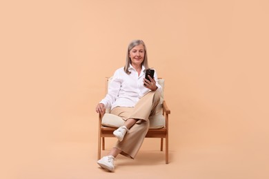 Photo of Senior woman with phone on armchair against beige background