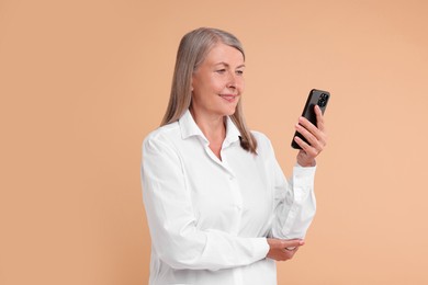 Senior woman with phone on beige background