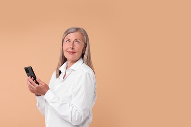 Senior woman with phone on beige background, space for text