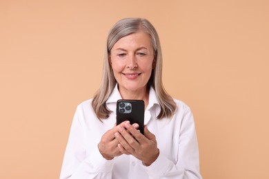 Senior woman with phone on beige background