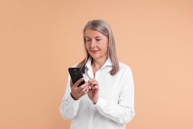 Senior woman with phone on beige background