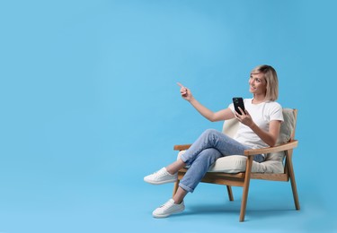 Photo of Happy woman with phone on armchair against light blue background, space for text