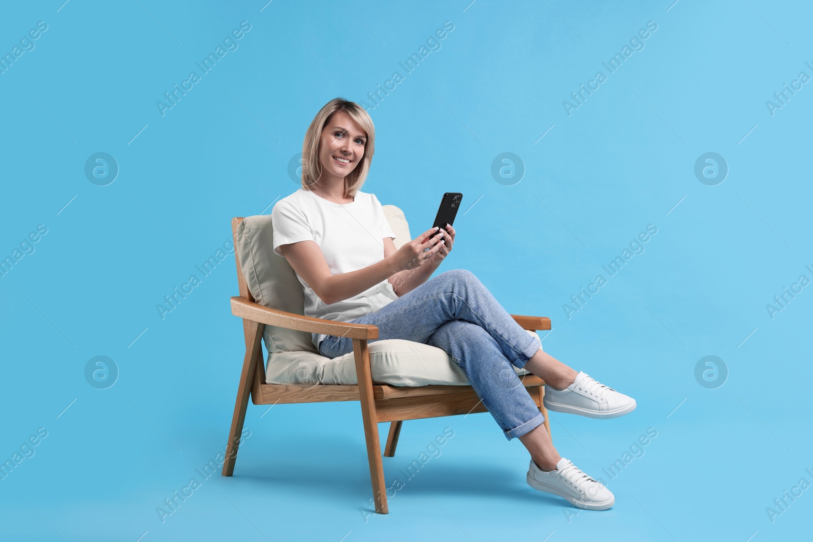 Photo of Happy woman with phone on armchair against light blue background