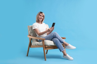 Happy woman with phone on armchair against light blue background