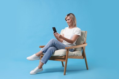 Photo of Happy woman with phone on armchair against light blue background