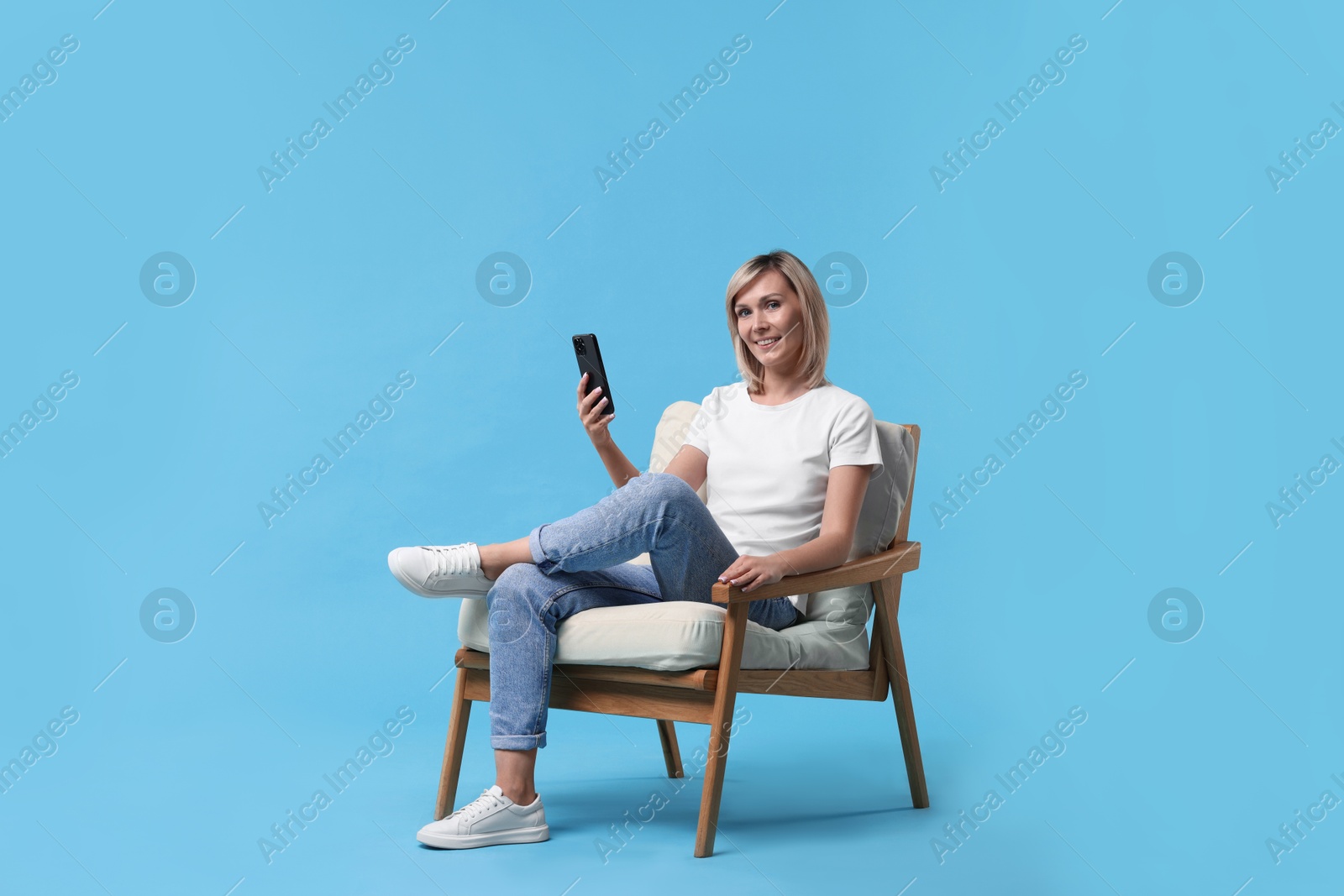 Photo of Happy woman with phone on armchair against light blue background