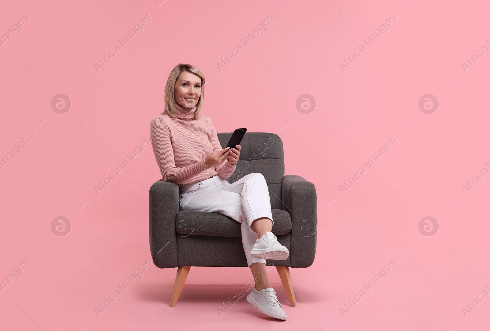 Photo of Happy woman with phone on armchair against pink background