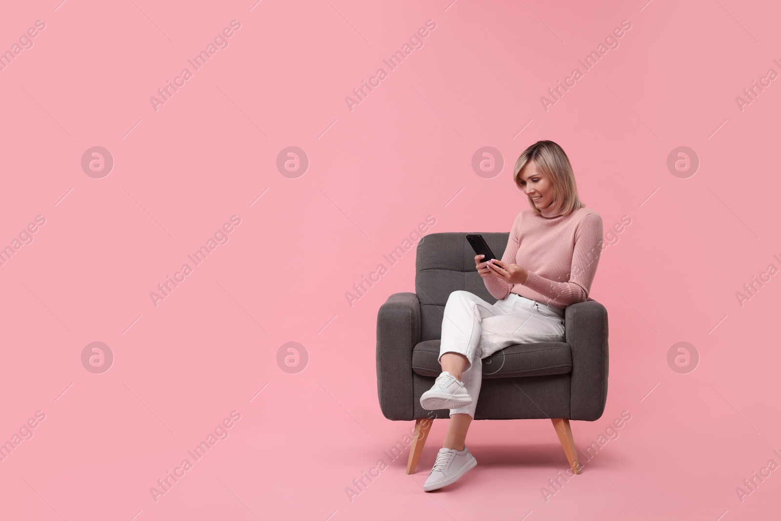 Photo of Happy woman with phone on armchair against pink background, space for text