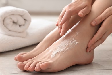 Photo of Woman applying moisturizing cream onto her feet on floor, closeup. Body care