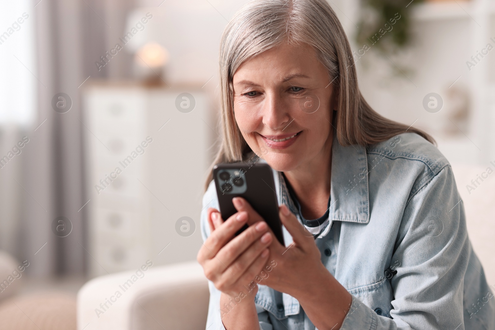 Photo of Senior woman using mobile phone at home, space for text