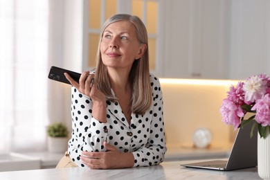 Senior woman using mobile phone at white table indoors