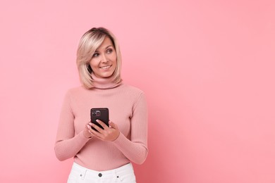 Photo of Happy woman with phone on pink background, space for text