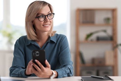 Photo of Happy woman using mobile phone at white table indoors, space for text