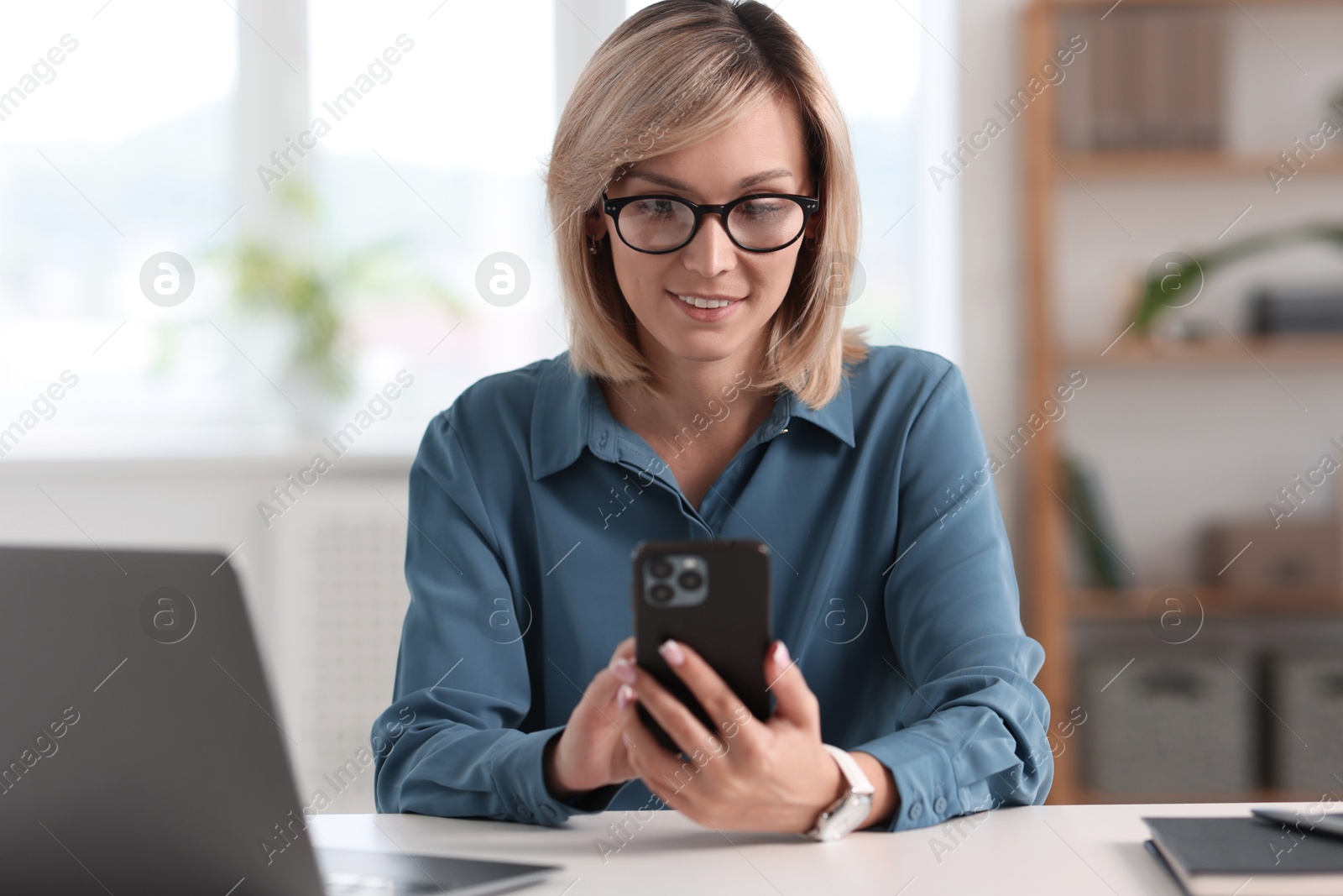 Photo of Happy woman using mobile phone at white table indoors