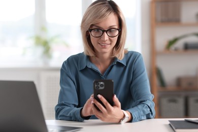 Happy woman using mobile phone at white table indoors