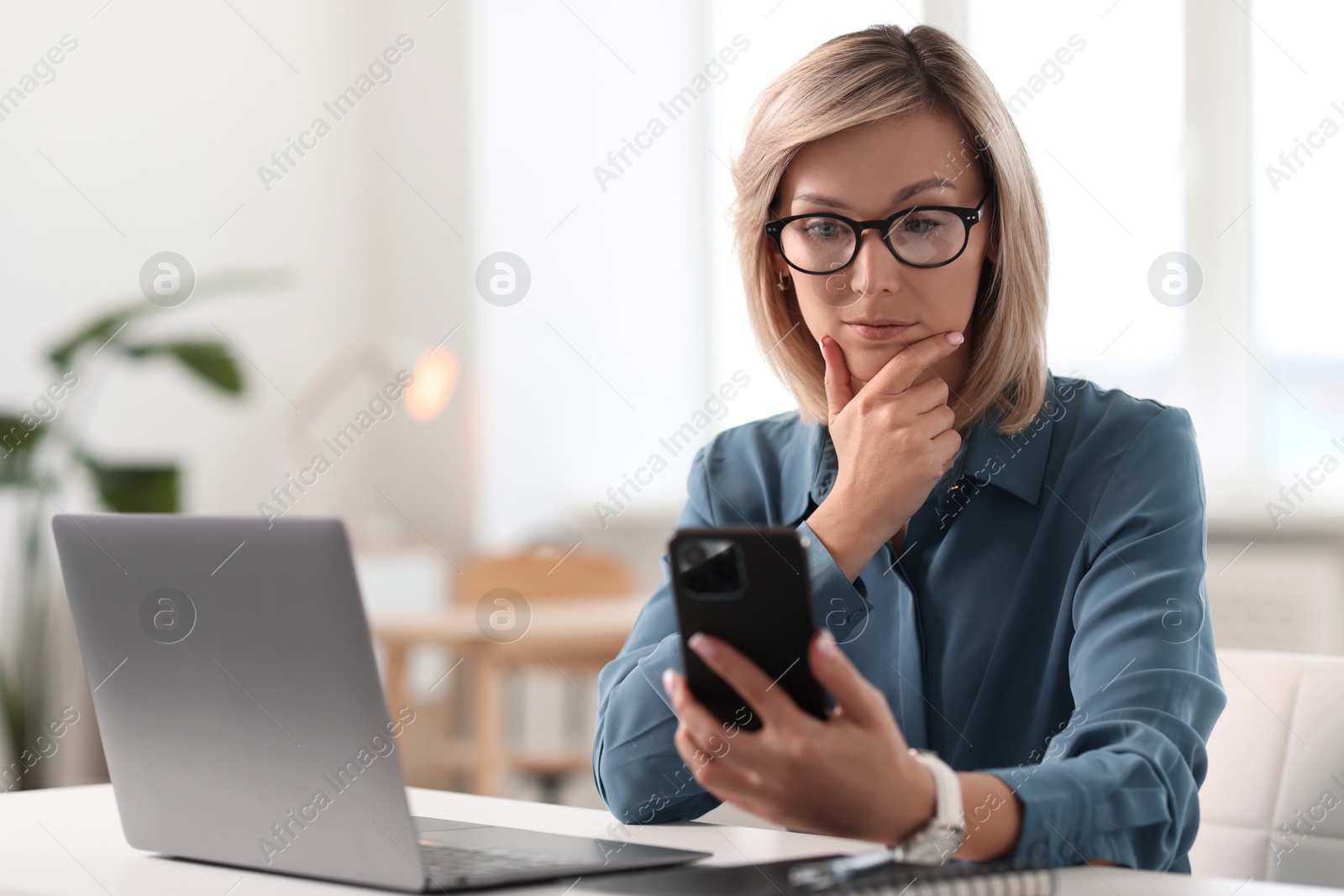 Photo of Woman using mobile phone at white table indoors