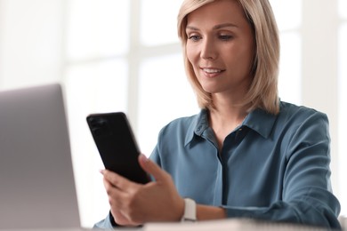 Photo of Happy woman using mobile phone at white table indoors