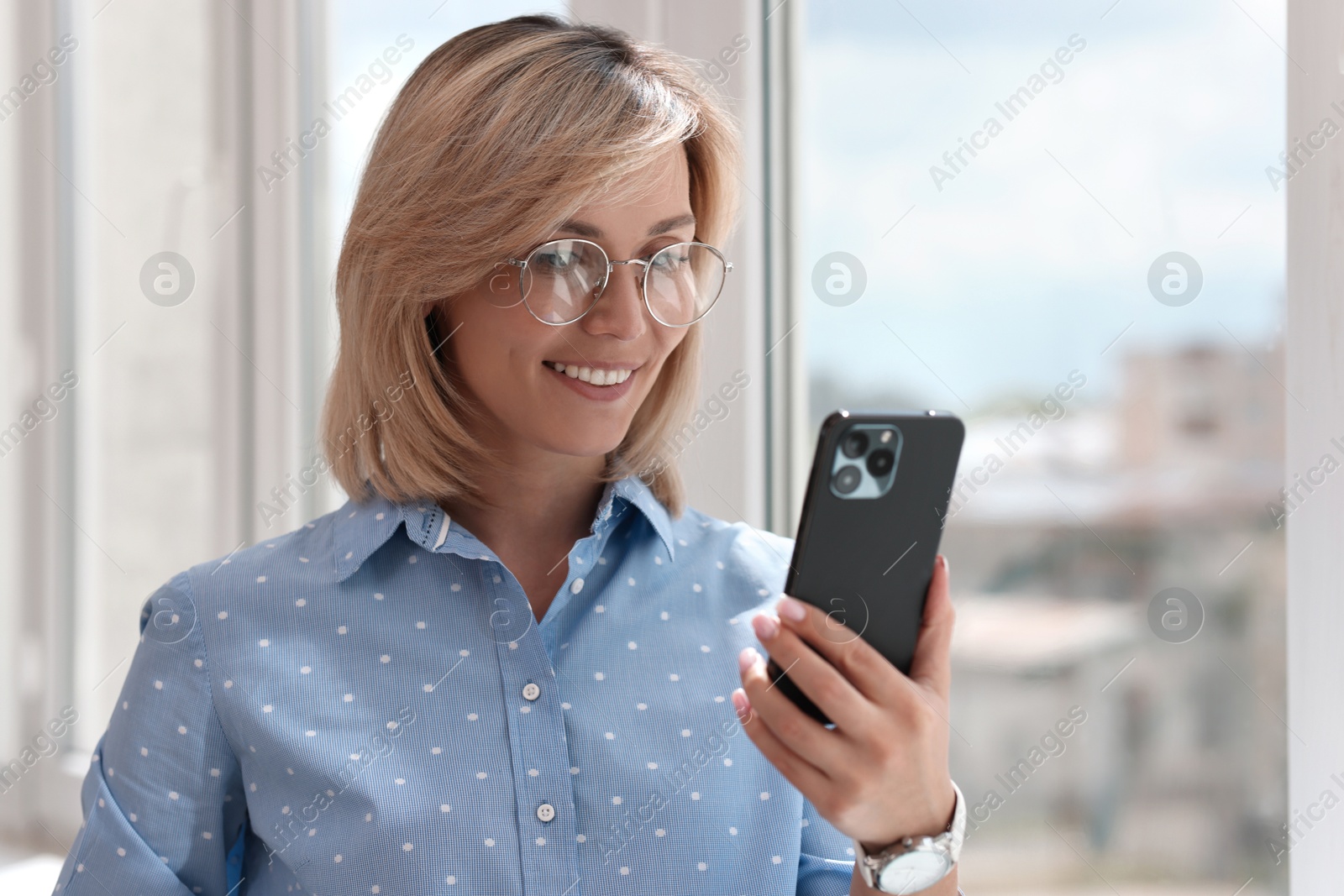 Photo of Happy woman using mobile phone near window indoors