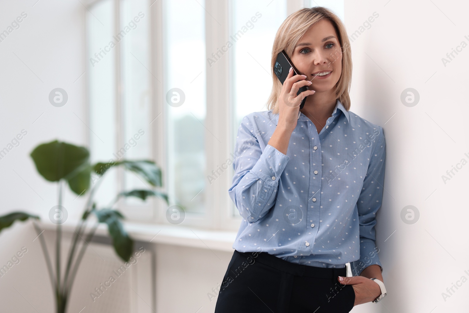 Photo of Happy woman talking on phone near window indoors, space for text