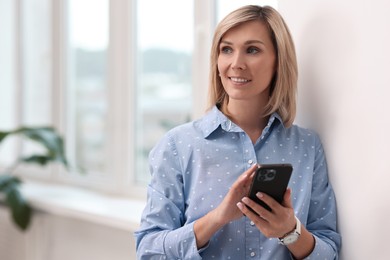 Photo of Happy woman using mobile phone near window indoors, space for text