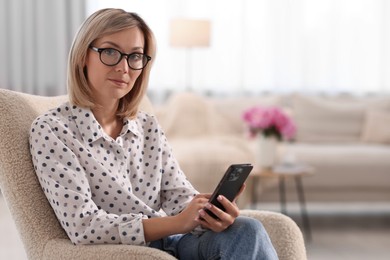 Woman with glasses using mobile phone at home, space for text