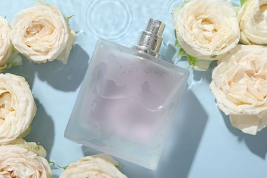 Photo of Beautiful rose flowers and perfume bottle in water on light blue background, flat lay