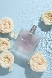 Photo of Beautiful rose flowers and perfume bottle in water on light blue background, flat lay