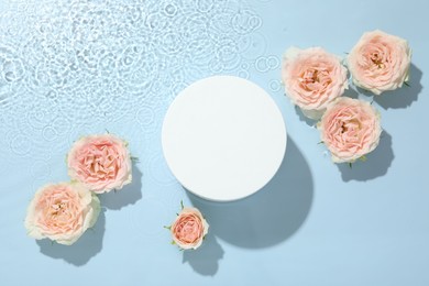 Beautiful rose flowers and round shaped podium in water on light blue background, flat lay