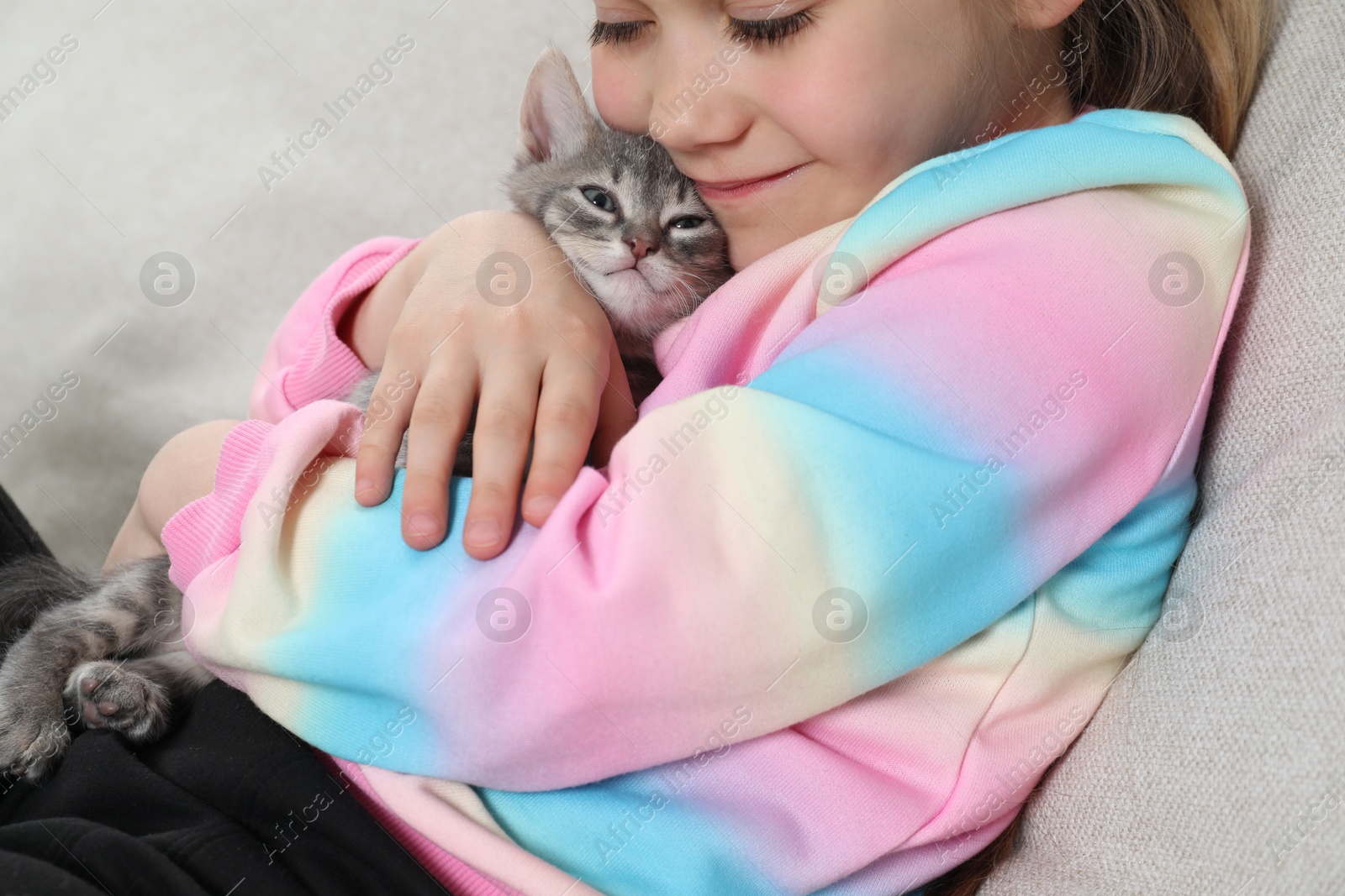 Photo of Little girl with cute fluffy kitten on sofa, closeup