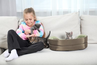 Photo of Little girl with cute fluffy kittens on sofa indoors