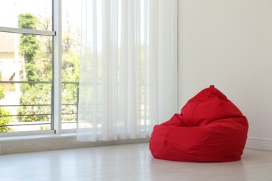 Photo of Red bean bag chair near window in room. Space for text