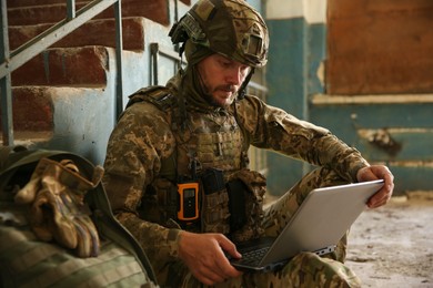 Photo of Military mission. Soldier in uniform using laptop inside abandoned building