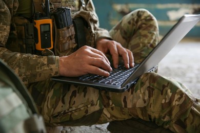 Photo of Military mission. Soldier in uniform using laptop inside abandoned building, closeup