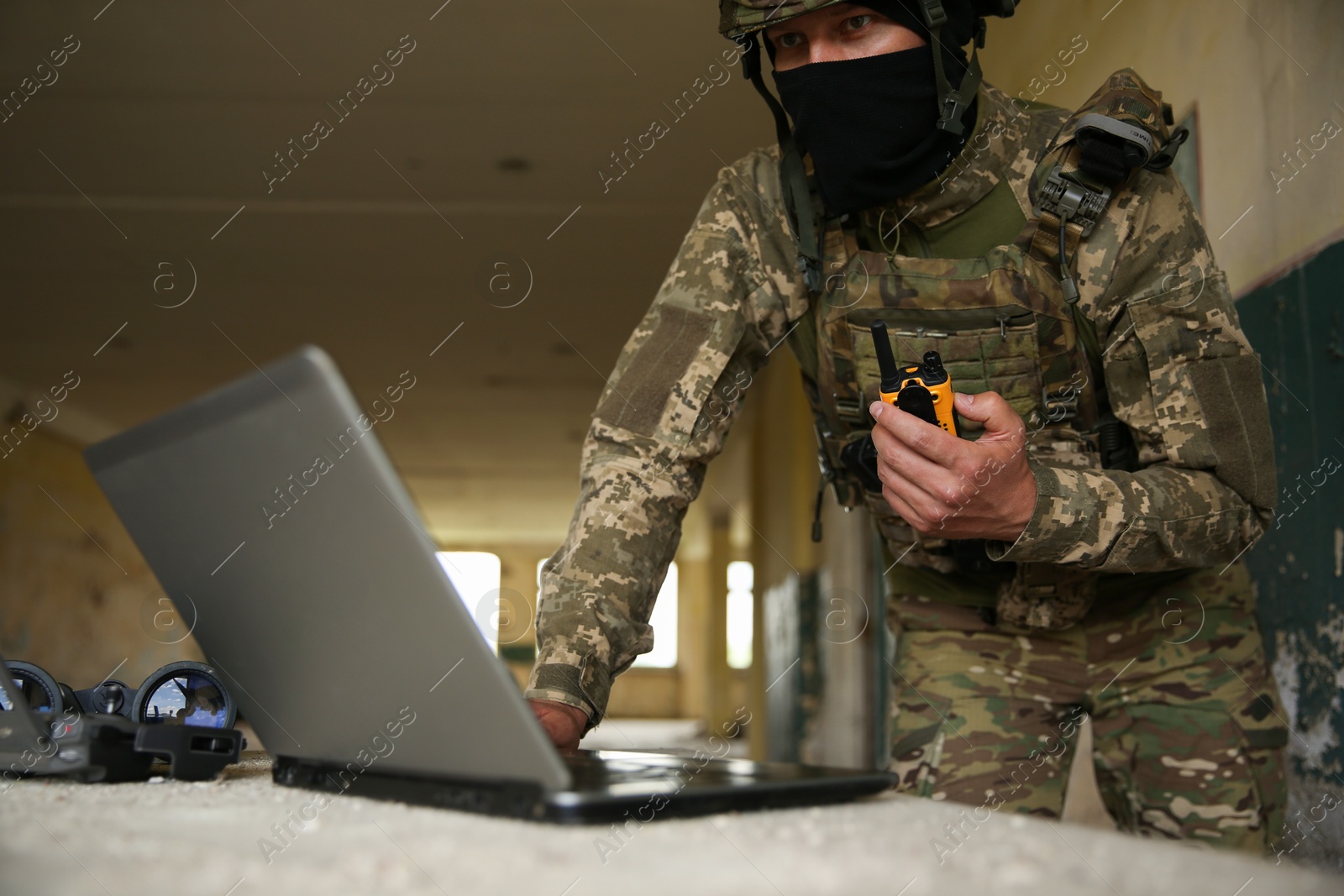 Photo of Military mission. Soldier in uniform with radio transmitter using laptop at table inside abandoned building