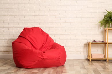 Photo of Red bean bag chair near white brick wall in room. Space for text