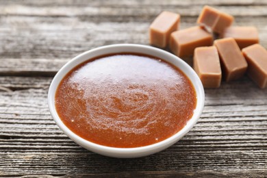 Yummy salted caramel sauce in bowl on wooden table, closeup