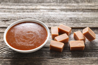 Photo of Salted caramel sauce in bowl and yummy candies on wooden table