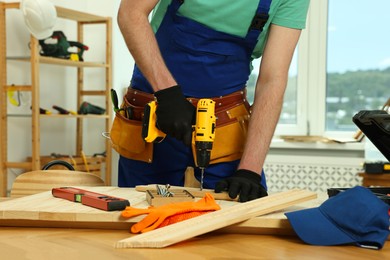 Craftsman working with drill at wooden table in workshop, closeup