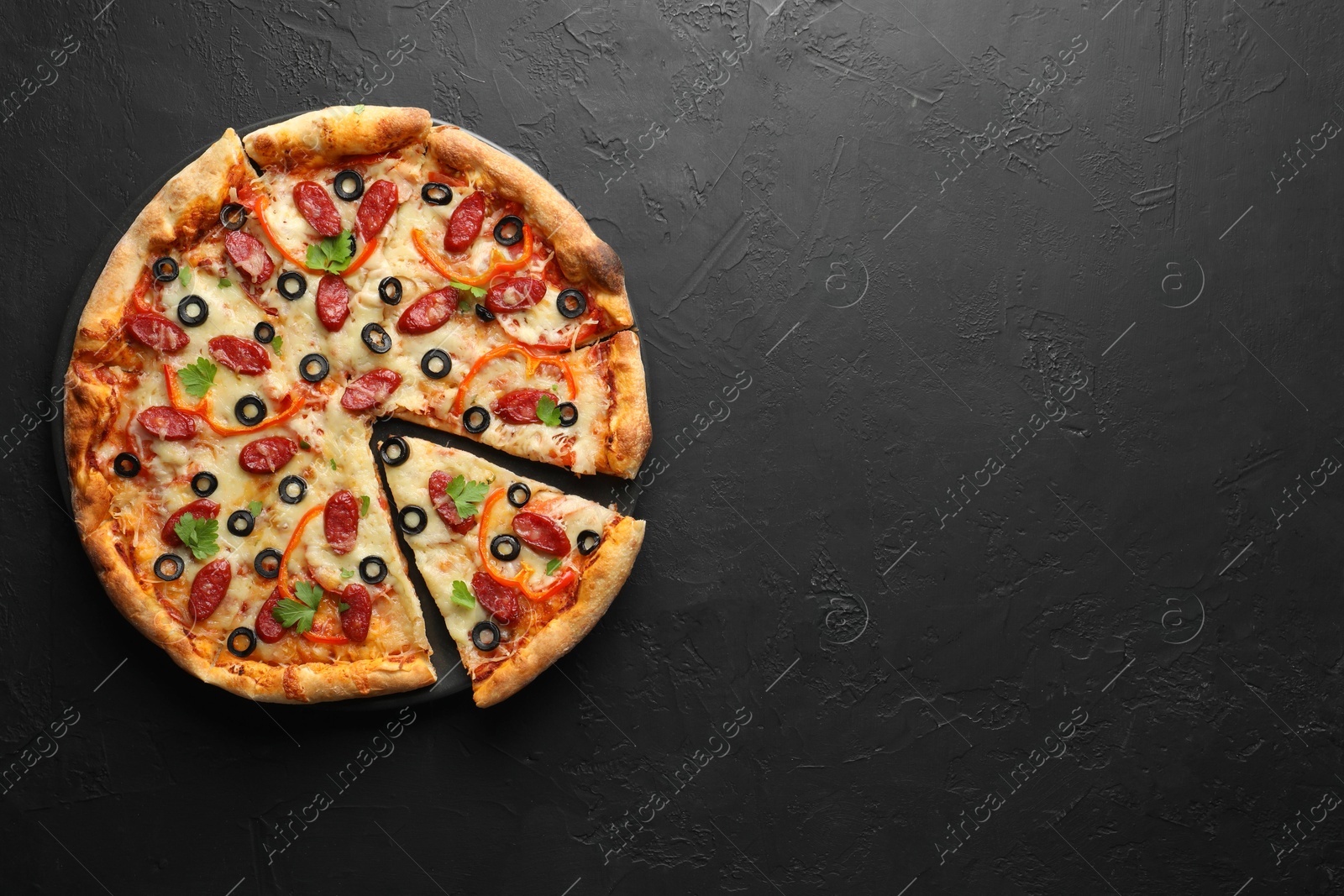 Photo of Tasty pizza with dry smoked sausages, olives, pepper and parsley on black table, top view. Space for text