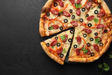 Tasty pizza with dry smoked sausages, olives, pepper and parsley on black table, top view. Space for text