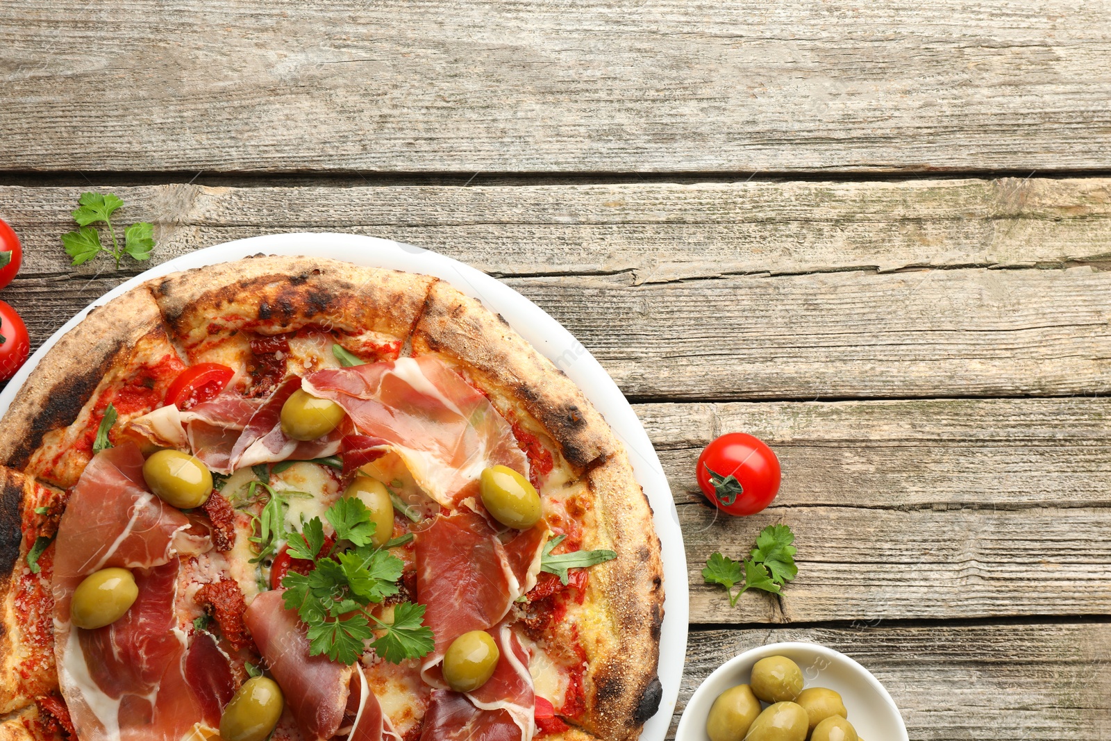 Photo of Tasty pizza with cured ham, olives, tomatoes and parsley on wooden table, top view. Space for text