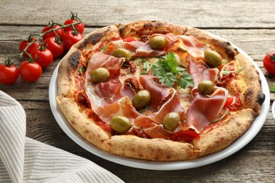 Photo of Tasty pizza with cured ham, olives, tomatoes and parsley on wooden table