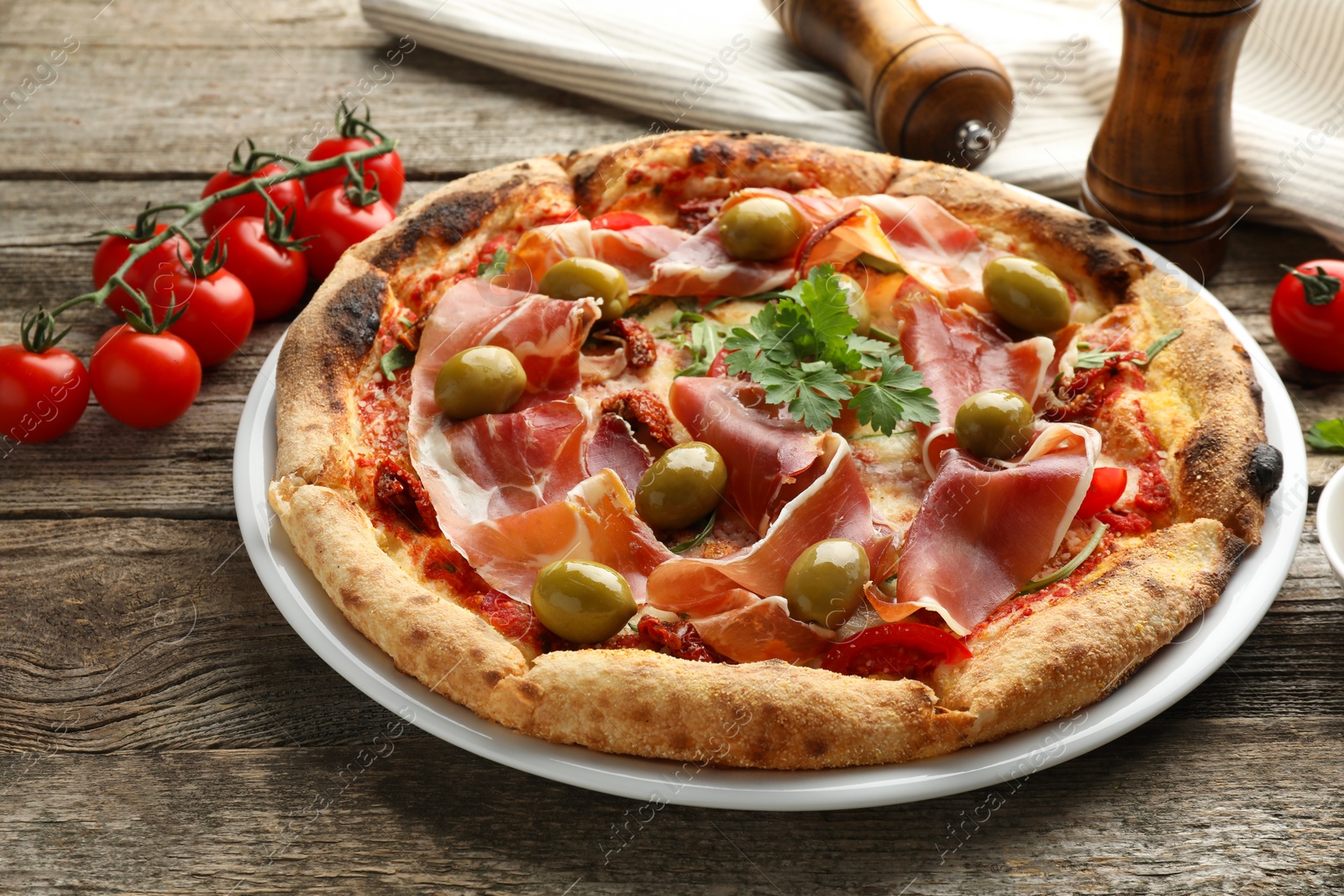 Photo of Tasty pizza with cured ham, olives, tomatoes and parsley on wooden table