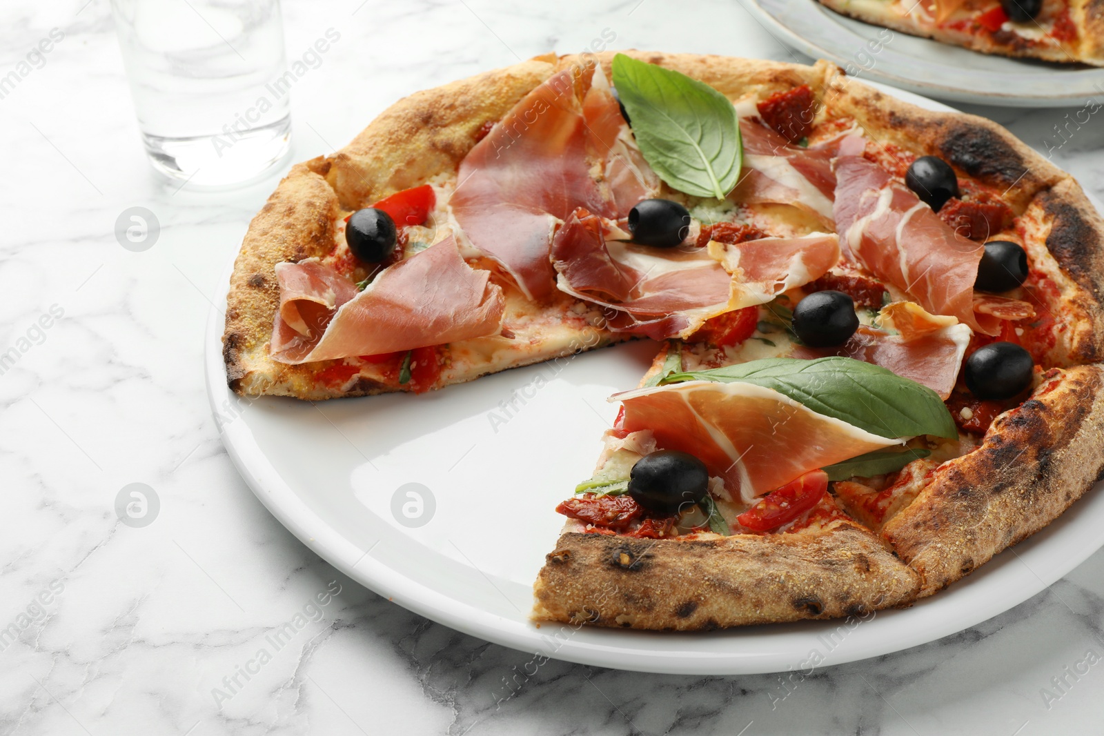 Photo of Tasty pizza with cured ham, olives, sun-dried tomato and basil on white table