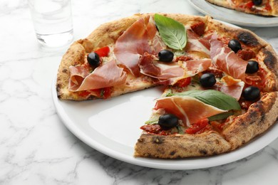 Tasty pizza with cured ham, olives, sun-dried tomato and basil on white table