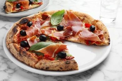 Tasty pizza with cured ham, olives, sun-dried tomato and basil on white table, closeup